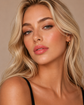 Blonde model wearing KDLR Beauty Labs Noir Patent Cream Lipstick in Darling Dahlia with luminous skin and soft peachy pink satin lips.