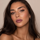 Brunette model wearing KDLR Beauty Labs Noir Patent Cream Lipstick in Magical Mauve with soft glam makeup and glowing skin.